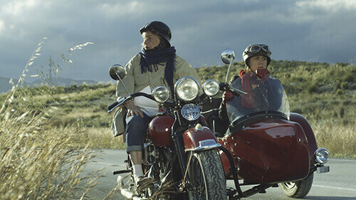 Imagen de producción de Marallavi Films con sidecars en carretera de campo con nubes oscuras.
